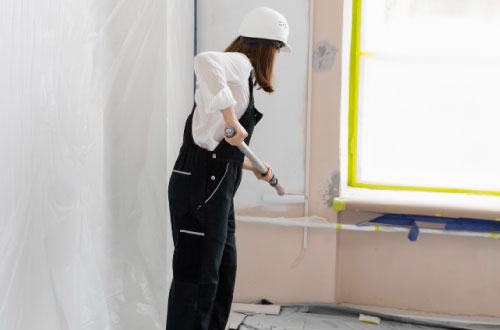 Une femme peint un mur intérieur avec un peinture blanche