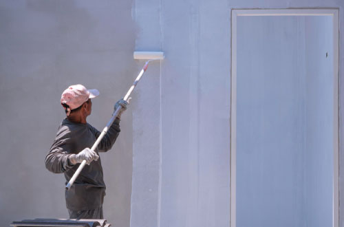 Peintre en bâtiment peignant le mur d'un immeuble en blanc